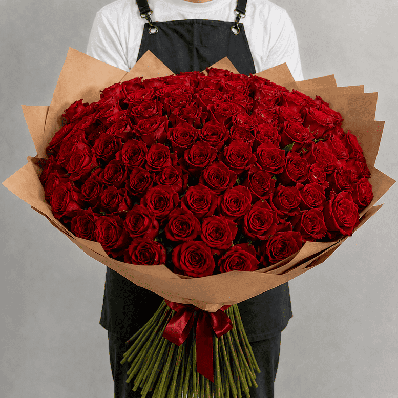 Person holding a large bouquet of red roses wrapped in brown paper against a gray background