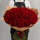Person holding a large bouquet of red roses wrapped in brown paper against a gray background