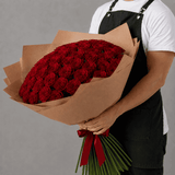 Person holding a large bouquet of red roses wrapped in brown paper with a red bow against a gray background