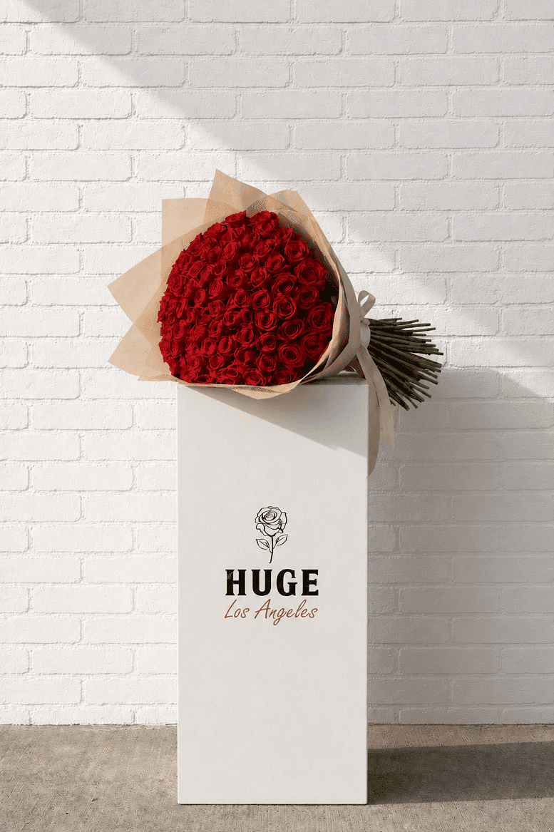 Bouquet of red roses wrapped in brown paper with 'HUGE Los Angeles' branding against a white brick wall.