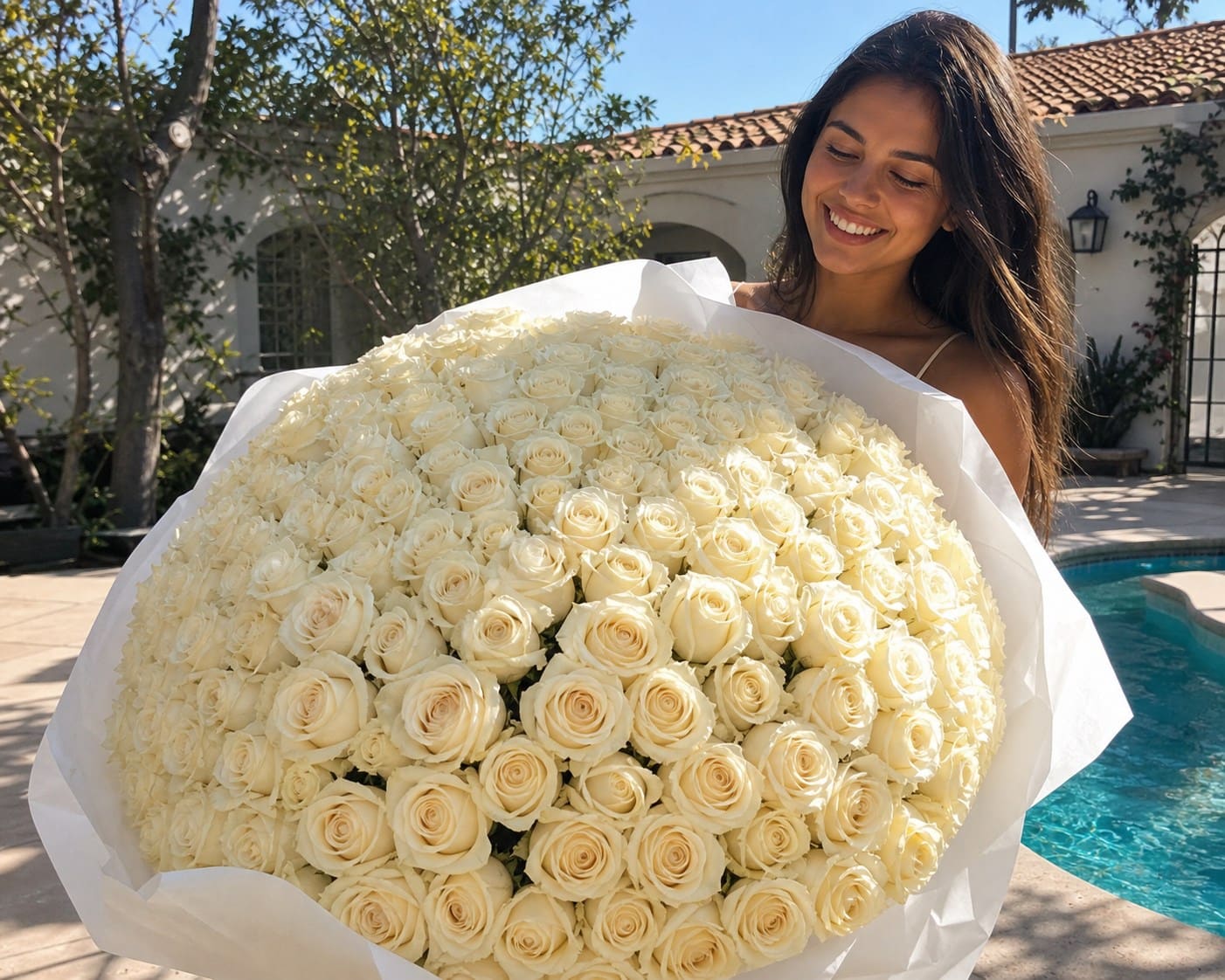 A smiling woman holding an oversized ivory rose bouquet by a pool